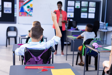 Diverse female teacher and boy with raised hand in class. Education, inclusivity, elementary school, learning concept.の写真素材