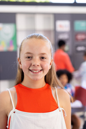 Vertical portrait of smiling caucasian school girl standing in classroom, copy space. Education,...