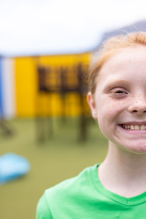 Vertical half face portrait of smiling caucasian schoolgirl in schoolyard, with copy space. Education, inclusivity, elementary school and learning concept.の写真素材