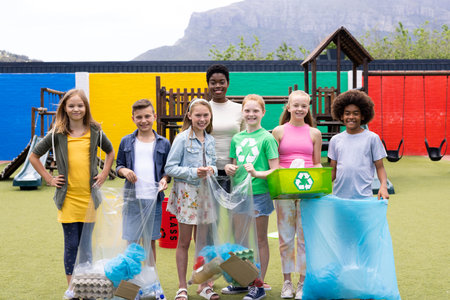Portrait of happy diverse female teacher and pupils holding recycling collected in schoolyard. Education, inclusivity, elementary school and learning concept.の写真素材