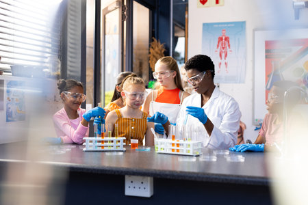 Diverse female teacher and schoolchildren doing an experiment in chemistry class. Education, inclusivity, elementary school and learning concept.の写真素材