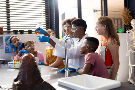 Diverse female teacher and school children doing experiment in chemistry class. Education, inclusivity, elementary school and learning concept.の写真素材