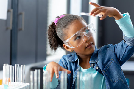 Happy biracial schoolgirl in safety glasses doing experiment in science class with copy space. Education, inclusivity, childhood, elementary school and learning concept.の写真素材