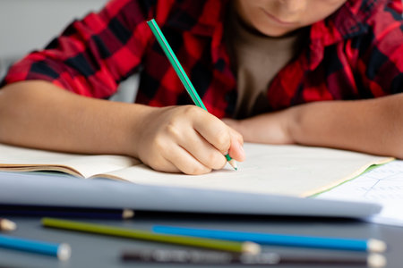 Midsection of caucasian schoolboy sitting at desk writing in class concentrating. Education, childhood, elementary school and learning concept.の写真素材