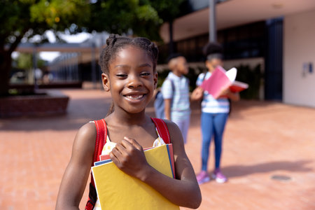 Portrait of happy african american schoolgirl standing in school yard. Education, childhood,...