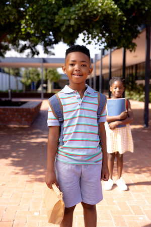 Portrait of happy african american schoolboy standing in school yard. Education, childhood, elementary school and learning concept.の写真素材