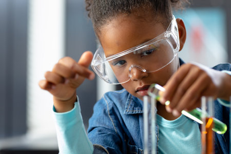 Serious biracial schoolgirl in safety glasses doing experiment in science class with copy space....