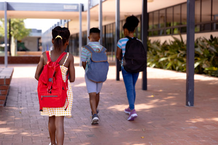 Happy african american schoolchildren wearing school bags and spending time in school yard. Education, childhood, elementary school and learning concept.の写真素材