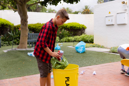 Happy caucasian schoolboy cleaning and recycling waste at school. Education, elementary school and learning concept.の写真素材