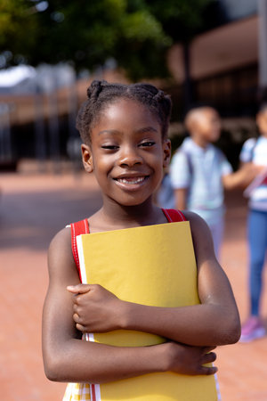 Portrait of happy african american schoolgirl standing in school yard. Education, childhood,...