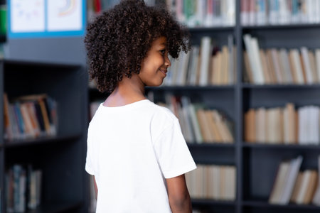 African american schoolboy wearing white t shirt with copyspace over library. Fashion, casual wear,...