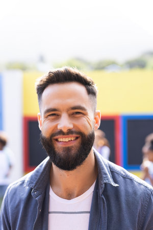 Vertical portrait of smiling, bearded caucasian male school teacher outdoors, with copy space....