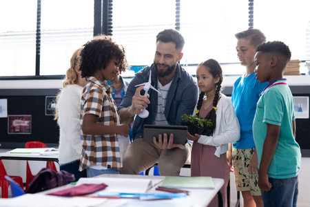 Diverse elementary schoolchildren and male teacher looking at wind turbine in classroom, copy space....