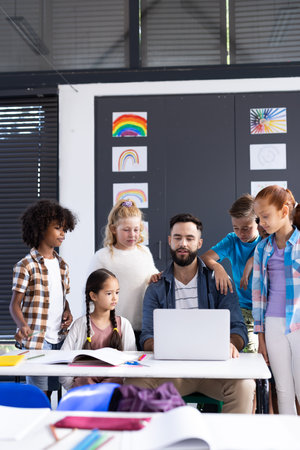 Vertical of diverse elementary schoolchildren and male teacher using laptop in classroom, copy space. Education, inclusivity, elementary school and learning concept.の写真素材