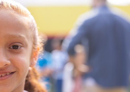Half face portrait of smiling biracial elementary schoolgirl in school playground, copy space. Education, inclusivity, elementary school and learning concept.の写真素材