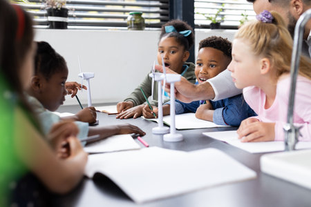 Diverse elementary schoolchildren and male teacher studying wind turbines in class, copy space....