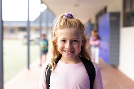 Portrait of smiling caucasian schoolgirl in elementary school corridor, with copy space. Education, inclusivity, elementary school and learning concept.の写真素材