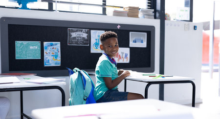 Smiling african american schoolboy at desk in elementary school classroom, with copy space....