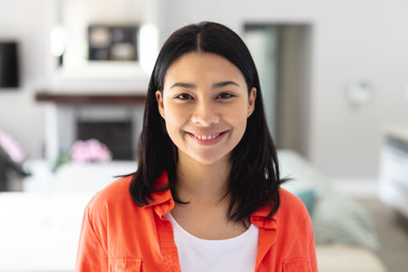 Portrait of happy biracial woman smiling in living room at home, with copy space. Leisure, happiness and domestic life concept.の写真素材