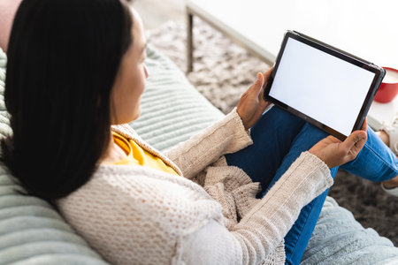 Asian woman sitting on sofa in living room and using tablet with copy space. Spending quality time at home and lifestyle concept.の写真素材
