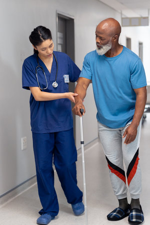 Vertical of diverse female doctor helping senior male patient use walking stick, copy space....