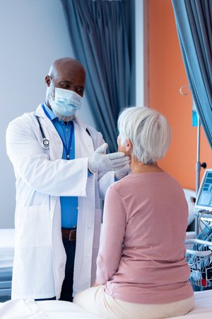 Vertical of diverse senior male doctor examining the throat of senior female patient, copy space....