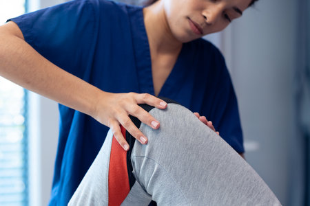 Smiling diverse female physiotherapist treating knee of senior male patient in therapy, copy space. Hospital, medical and healthcare services.の写真素材