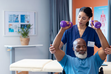 Diverse female physiotherapist helping senior male patient exercise with dumbbells, copy space. Hospital, medical and healthcare services.の写真素材