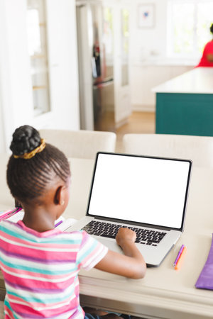 Rear view of african american girl with hair bun using laptop while studying on table at home. Copy...