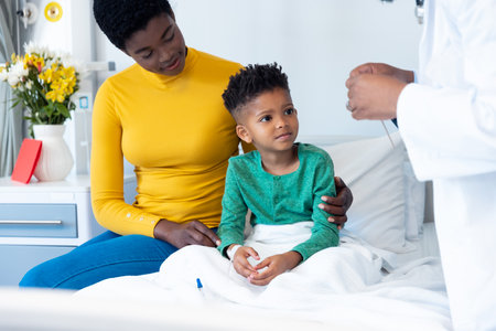 Smiling african american son patient with mother and male doctor in hospital. Hospital, medical and healthcare services.の写真素材