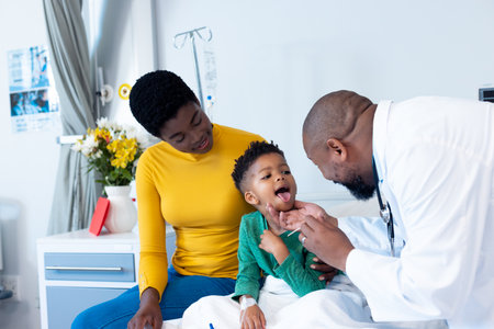 African american male doctor examining mouth of boy patient with mother in hospital. Hospital, medical and healthcare services.の写真素材