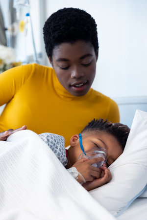 Vertical of african american mother beside son patient on ventilator in hospital bed with copy...