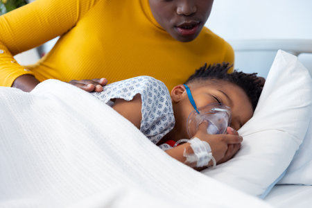African american mother lying beside son patient on ventilator in hospital bed with copy space. Hospital, medical and healthcare services.の写真素材