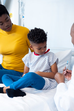 Vertical of african american male doctor showing vaccine to boy patient with mother and copy space. Hospital, medical and healthcare services.の写真素材