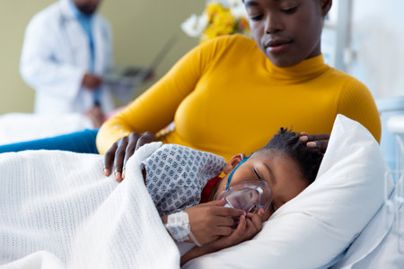 African american mother beside son patient on ventilator asleep in hospital bed. Hospital, medical...