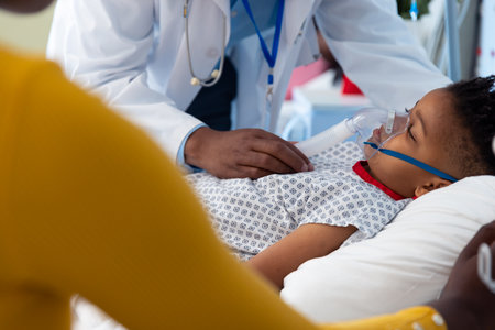 African american male doctor and mother beside son patient on ventilator in hospital bed. Hospital,...