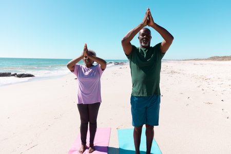 African american senior couple meditating in mountain pose at beach against clear sky. Copy space, summer, unaltered, love, together, yoga, retirement, nature, vacation and active lifestyle.の写真素材