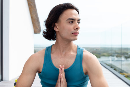 Happy biracial man doing yoga, meditating on balcony. Spending quality time at home alone, domestic life and lifestyle concept.の写真素材