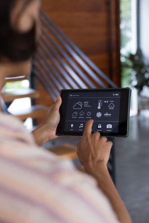 Vertical of hands of biracial man at home using tablet with smart home interface, copy space....