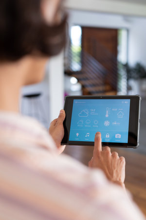 Vertical of hands of biracial man at home using tablet with smart home interface, copy space. Communication, technology and domestic life concept.の写真素材