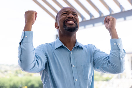 Happy african american businessman raising hands outside modern office. Global business, celebration and office concept.の写真素材