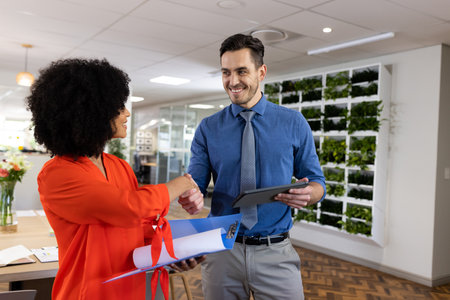 Diverse female and male businesspeople smiling and shaking hands in office. Business, corporation,...