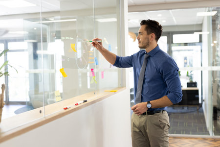 Focused caucasian man working and writing on glass board in office. Business, corporation, working...