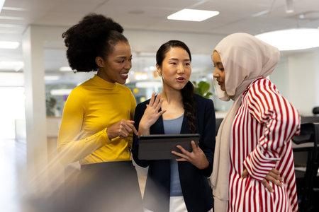 Vertical diverse businesswomen with tablet working and talking in office. Business, corporation, working in office and cooperation concept.の写真素材
