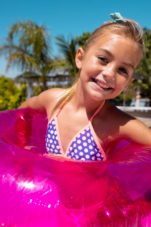 Portrait of happy biracial girl smiling and holding swim ring by the swimming pool. Spending quality...