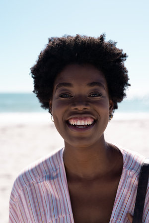 Closeup of happy african american mid adult woman with afro hair enjoying at beach under clear sky....