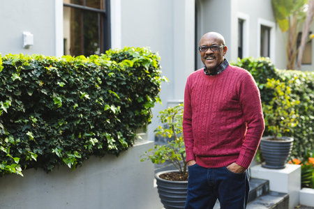 Portrait of happy senior african american man wearing glasses standing outside house, copy space....