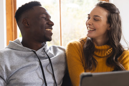 Happy diverse couple sitting on sofa using tablet at home. Lifestyle, togetherness, relationship, communication and dometic life, unaltered.の写真素材