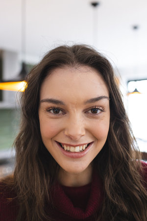 Portrait of happy caucasian woman with long brown hair smiling in kitchen at home. Lifestyle and...