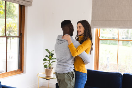 Happy diverse couple dancing in living room at home. Lifestyle, togetherness, relationship, romance and dometic life, unaltered.の写真素材